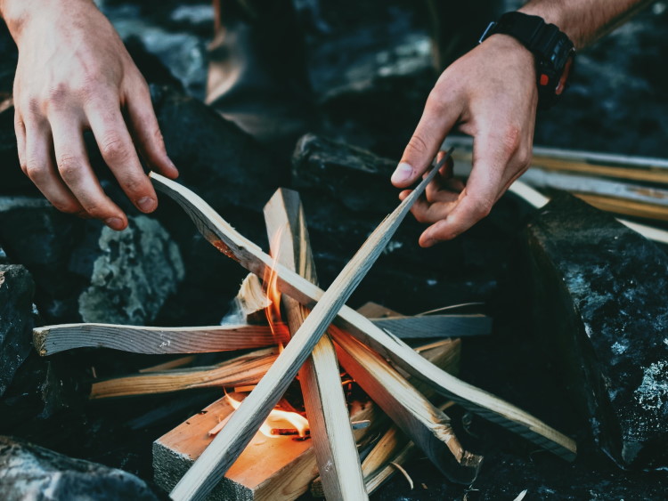 Hände richten Holz am Lagerfeuer aus