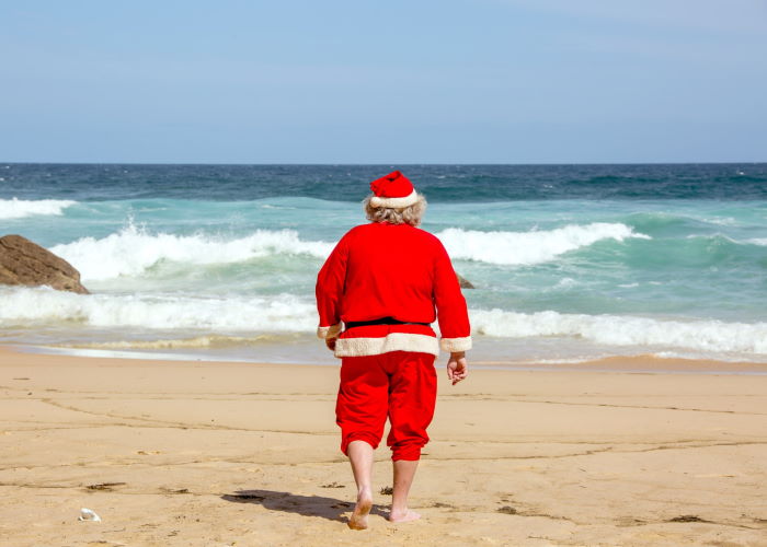 Vista trasera de una persona con un disfraz de Papá Noel en la playa
