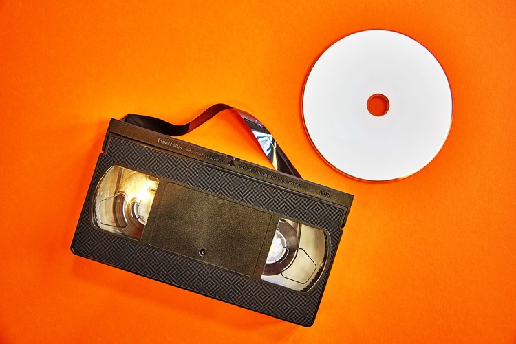 Una cinta de vídeo y un CD sobre fondo naranja.