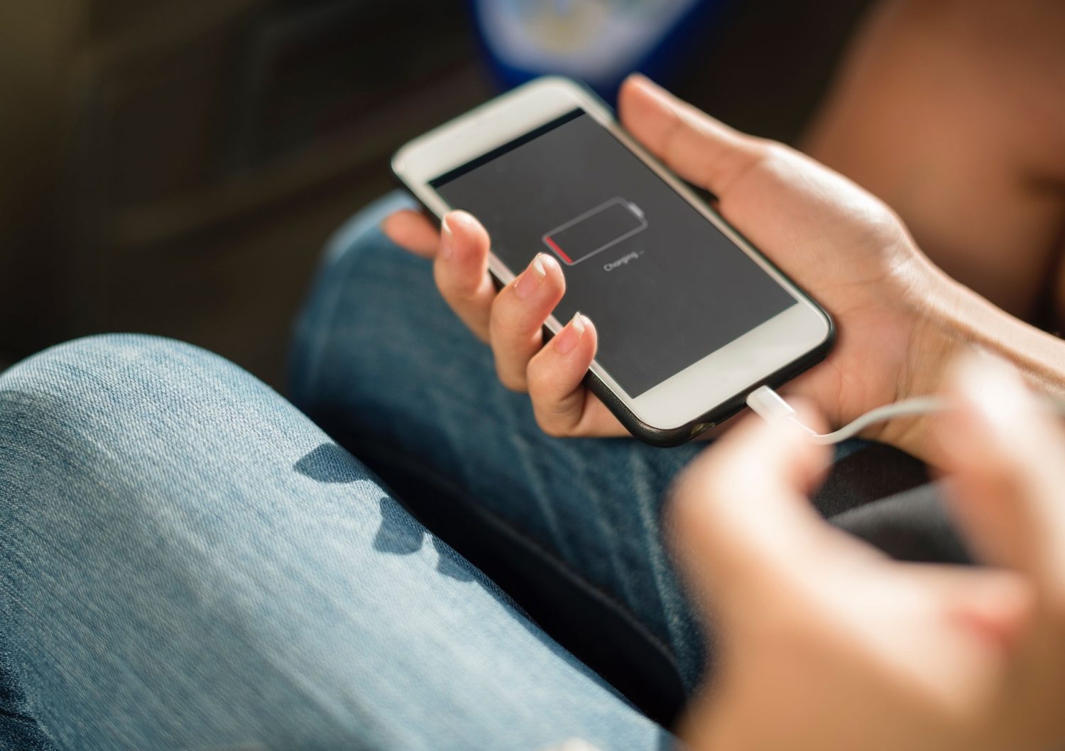 Person hält Smartphone mit niedrigem Akkustand und angeschlossenem Ladekabel in der Hand